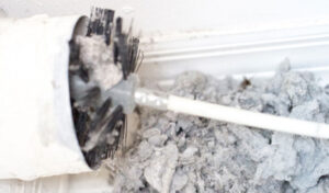 Dryer vent being cleaned, with a large amount of lint and debris being removed by a brush.